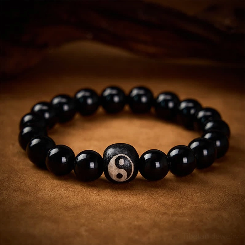 Close-up eye-level shot of Yin Yang beaded bracelet, single engraved Yin Yang bead among uniform black stone beads with dark wood background