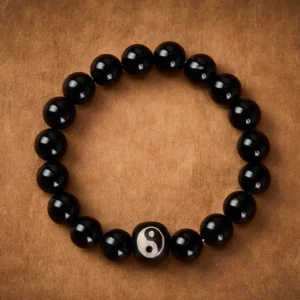 Black Onyx and Obsidian beaded bracelet overhead view, central Yin Yang decorated stone bead on brown leather surface