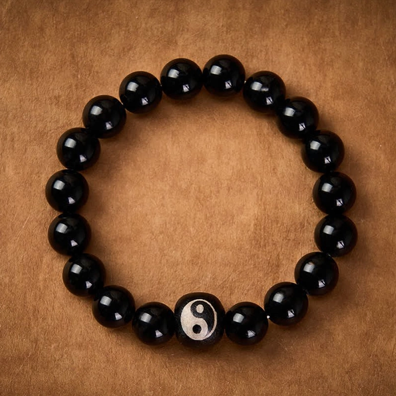 Black Onyx and Obsidian beaded bracelet overhead view, central Yin Yang decorated stone bead on brown leather surface