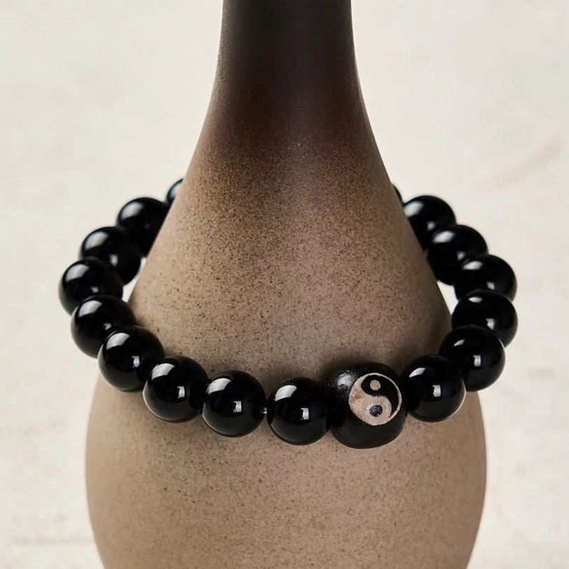 Black stone Yin Yang protection bracelet wrapped around ceramic vase, side product shot showing central engraved bead detail
