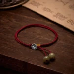 Handcrafted Tibetan Yin Yang sterling silver and red string protection bracelet with adjustable cord, displayed on dark wooden surface with ancient calligraphy paper