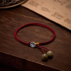 Handcrafted Tibetan Yin Yang sterling silver and red string protection bracelet with adjustable cord, displayed on dark wooden surface with ancient calligraphy paper
