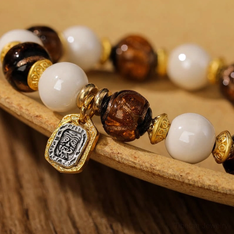 Close-up macro view of Tibetan charm bracelet showing glazed porcelain beads, gold metal spacers and engraved pendant