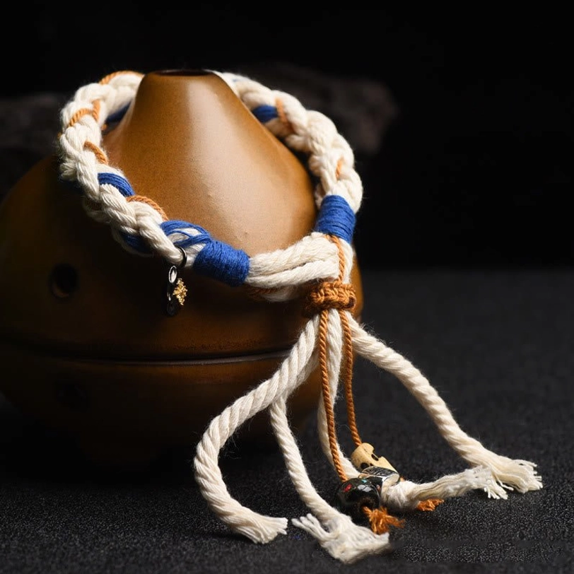 Handmade Zakiram wealth bracelet with blue-brown-white braided cord and metal charm accents on ceramic ornament