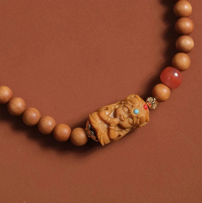 Close detail of Zakiram wealth bracelet showing sandalwood beads, red agate accent, carved wooden deity pendant with metal spacer
