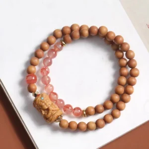 Double-loop Zakiram protection bracelet featuring pink South Red Agate beads separated with sandalwood, wooden carved deity centerpiece, flat lay
