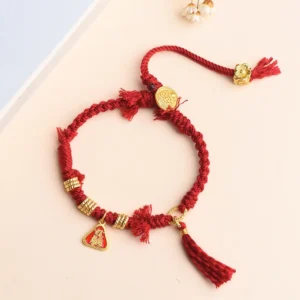 Tibetan red protection bracelet flat lay with gold round charm, tassel pendant, and red triangular tag