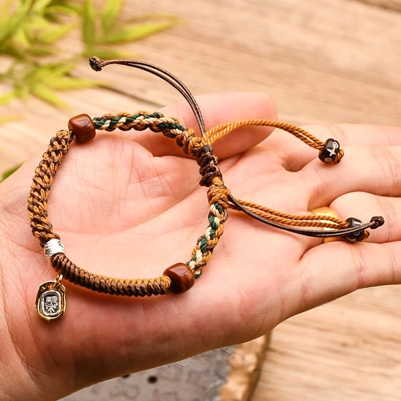 Tibetan Zakiram protection bracelet held in palm showing woven brown cords, wooden beads, and sacred metal pendant