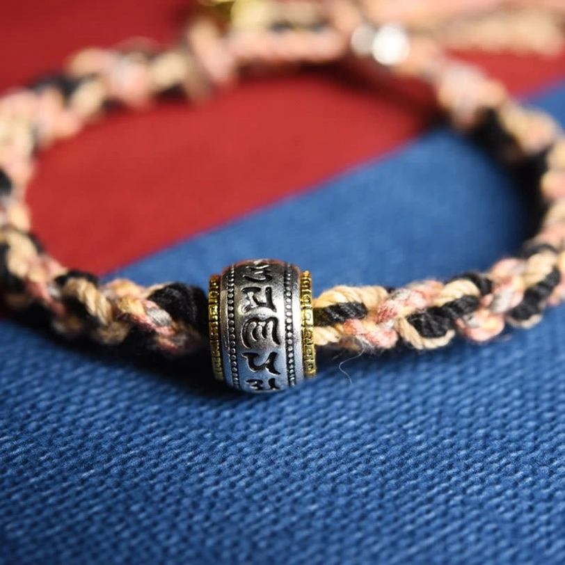 Close-up macro shot of Tibetan Zakiram bracelet engraved silver om mani padme hum mantra bead brown black braided rope and metal accents