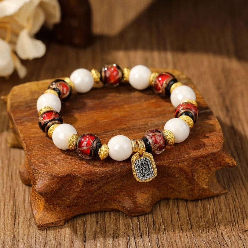 Red-toned Tibetan wealth goddess bracelet with white porcelain beads and red liuli glass on wooden stand