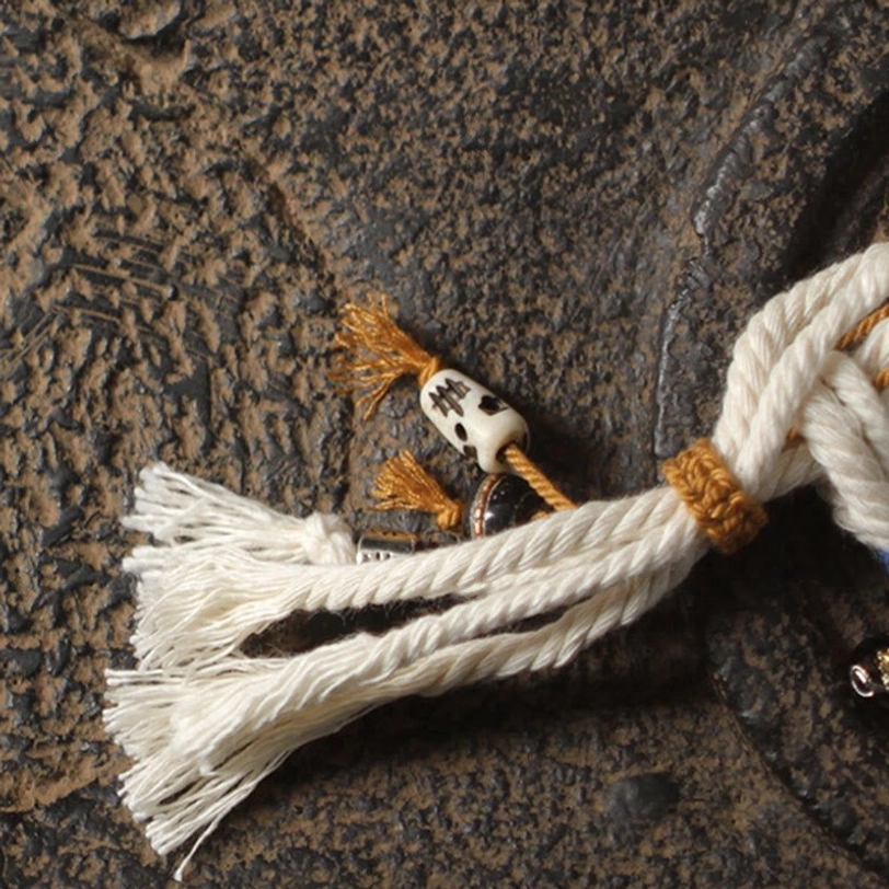 Zakiram wealth bracelet pendant detail featuring skull-shaped charm, brown rope knot, and white cotton tassel decoration