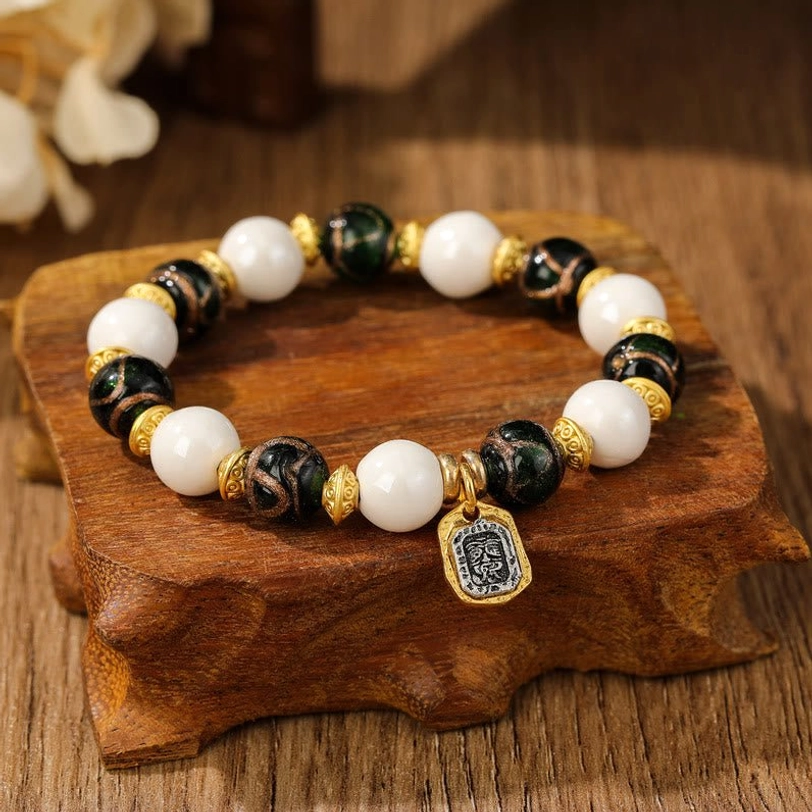 White and dark brown Tibetan Zakiram bracelet with glazed beads and gold metal accents on wooden display stand