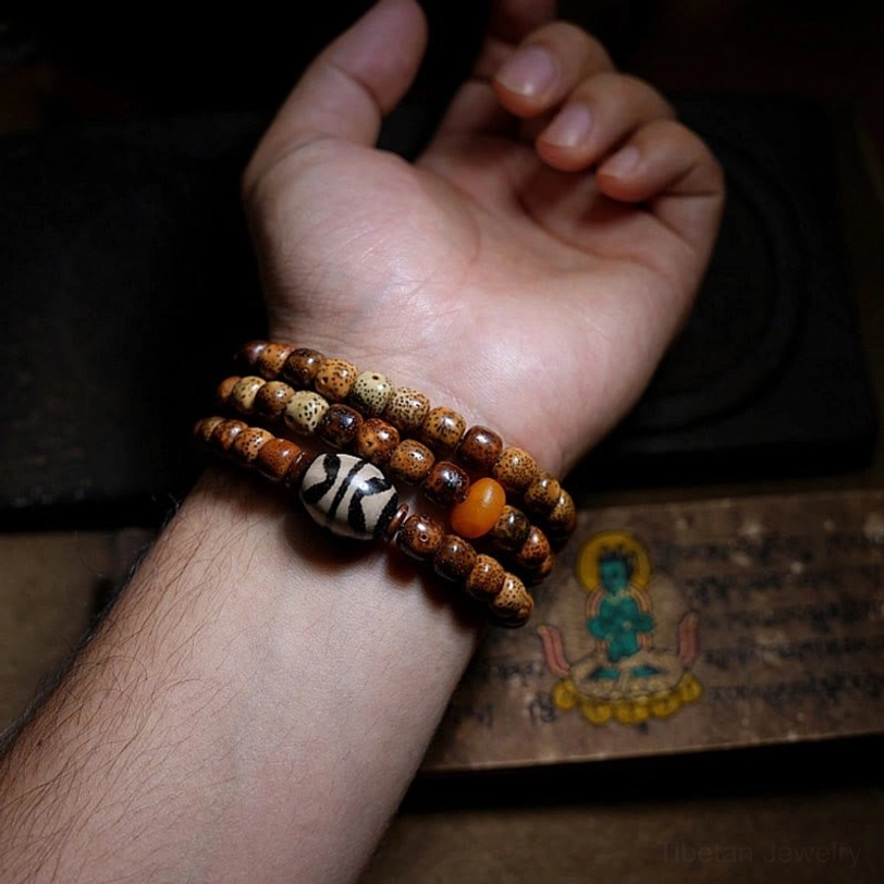 Zakiram wealth bracelet triple wrapped on human wrist with mixed bodhi and agate dzi beads near Tibetan religious artifacts