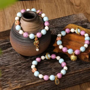 Multiple Zakiram Goddess wealth bracelets with various enamel charms and incense ash porcelain beads displayed on rustic wooden table
