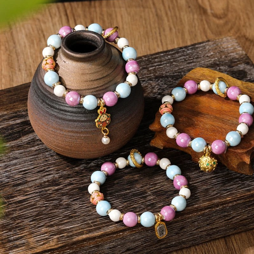 Multiple Zakiram Goddess wealth bracelets with various enamel charms and incense ash porcelain beads displayed on rustic wooden table