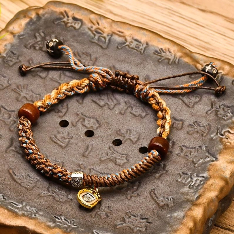 Brown Zakiram tibetan braided protection bracelet with wooden beads, metal pendant on carved stone background