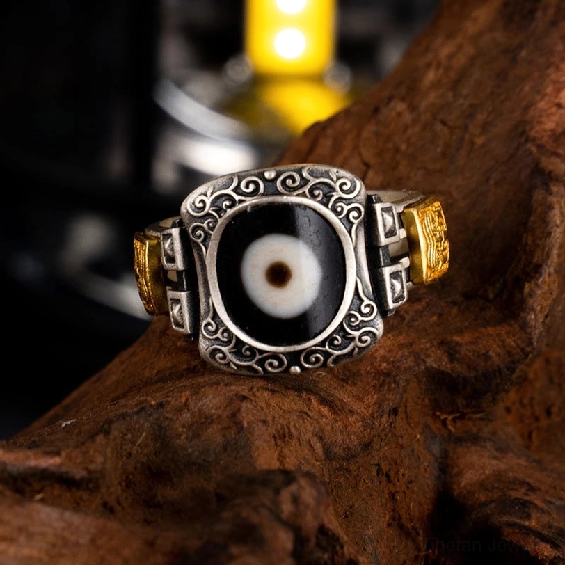 Zakiram wealth protection ring top view showcasing hand-painted Dzi bead center stone with embossed scroll frame and sterling silver setting