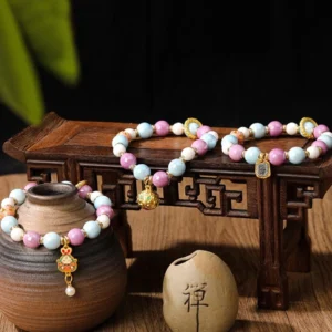Zakiram Goddess of Wealth bracelet with enamel rabbit charm and liuli glass beads in pastel pink and blue, overhead view on vintage wooden table