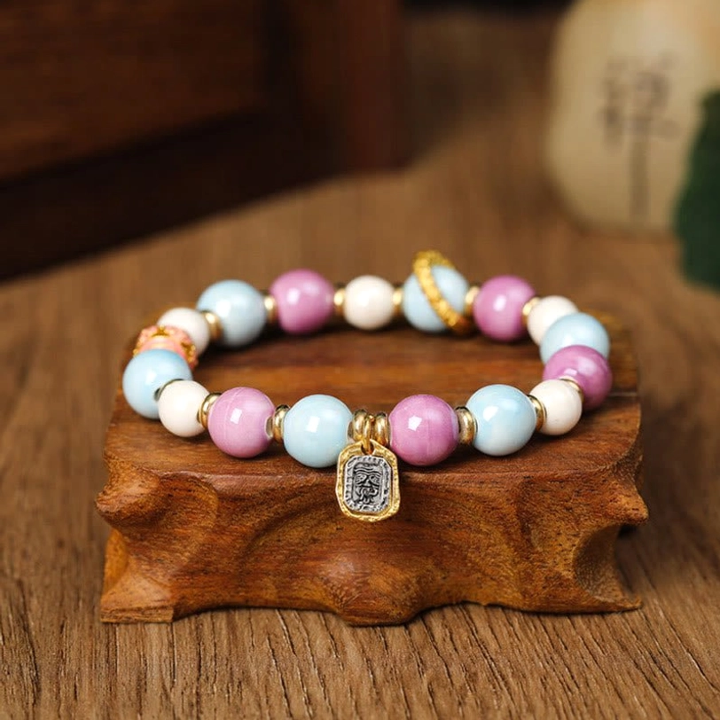 Zakiram Goddess of Wealth bracelet with engraved square metal pendant charm and pastel liuli glass beads, overhead view