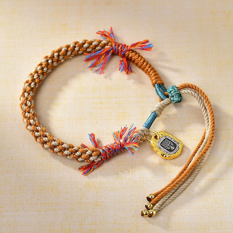 Tibetan Zakiram goddess wealth protection bracelet with multicolor braided rope, copper charm, and gold beads - side overhead view