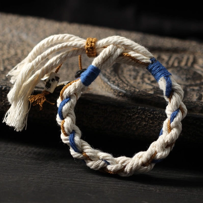 Tibetan luck bracelet handwoven with cotton rope, blue and brown accent wraps, and pendant charms on wooden surface