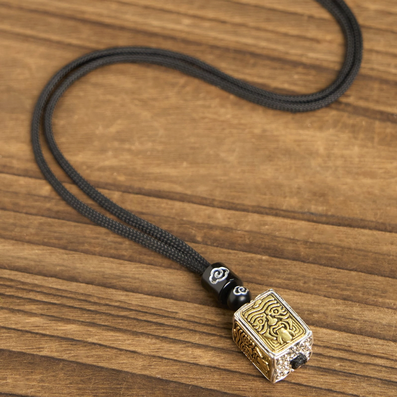 Full Zakiram tibetan goddess of wealth protection necklace set, complete length flat lay showing long black woven rope with cloud-patterned beads and square bicolor relief pendant