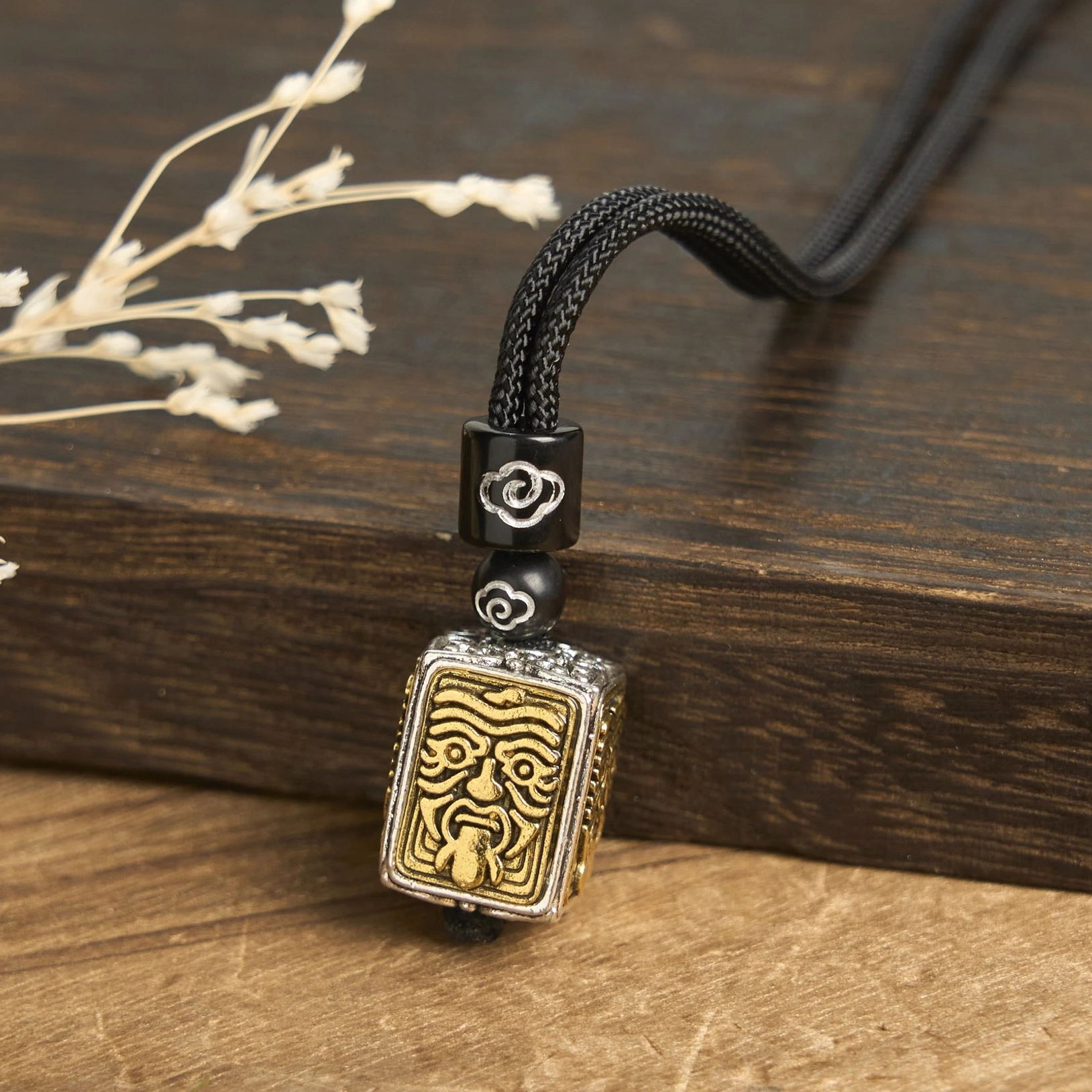 Zakiram fierce protector tibetan deity pendant necklace side angle view, showing intricate relief carving with black braided cord and cloud-patterned spacer beads