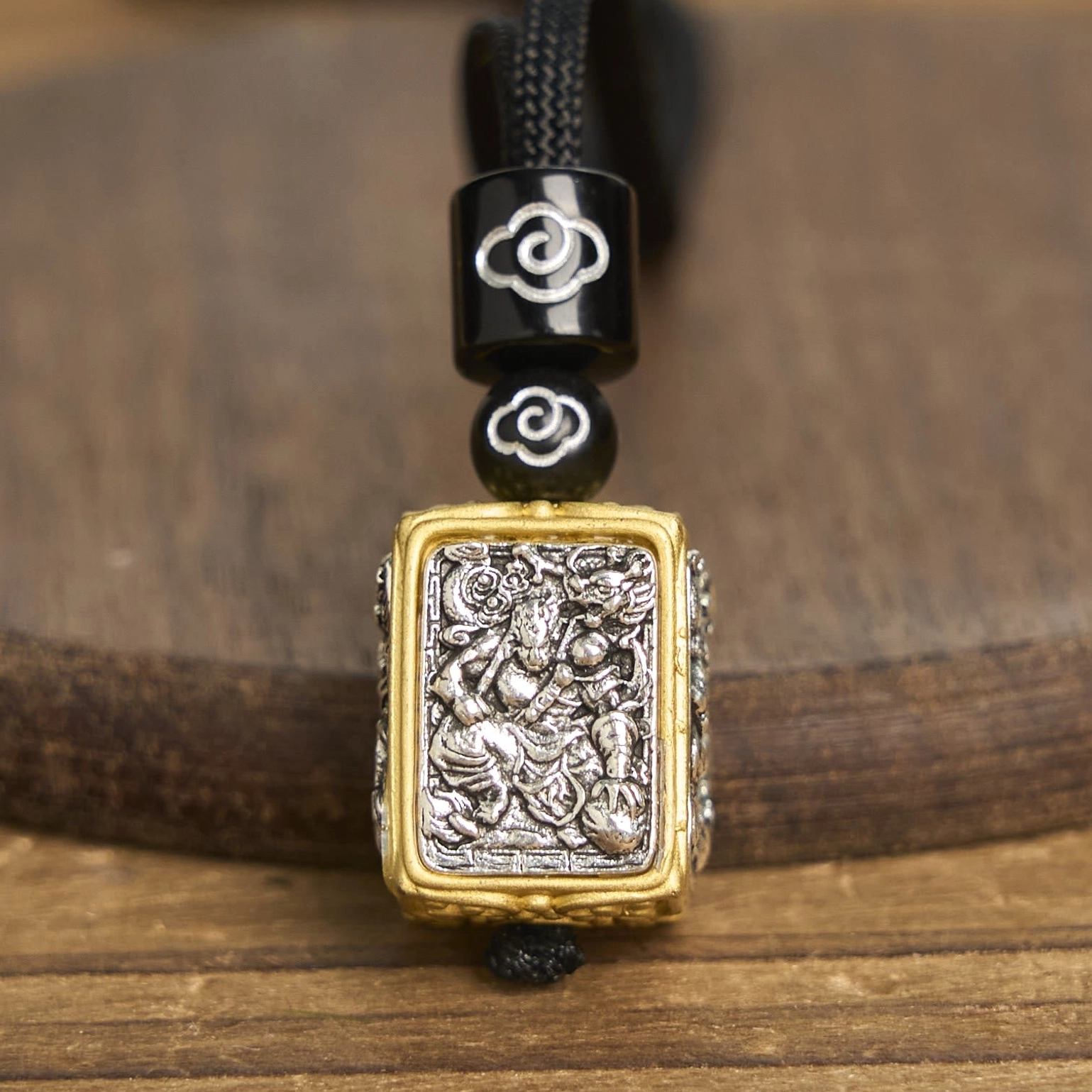 Zakiram tibetan protection pendant amulet detailed close-up front view, featuring silver deity carving with gold-silver bicolor frame and cloud-patterned black decorative beads