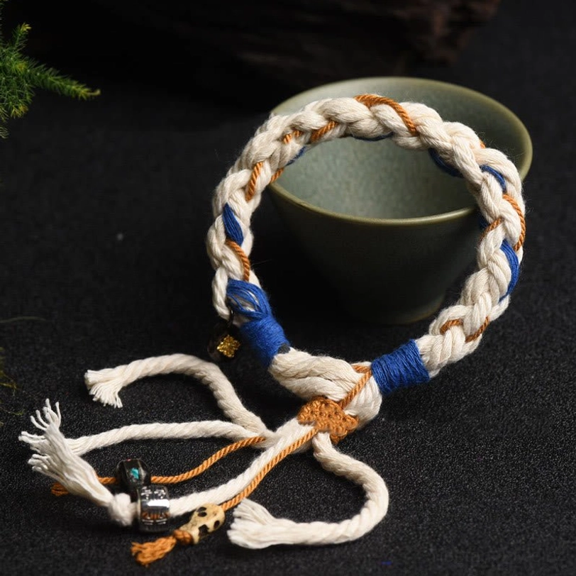 Tibetan Zakiram bracelet with woven cotton rope and decorative tassels displayed on green ceramic bowl
