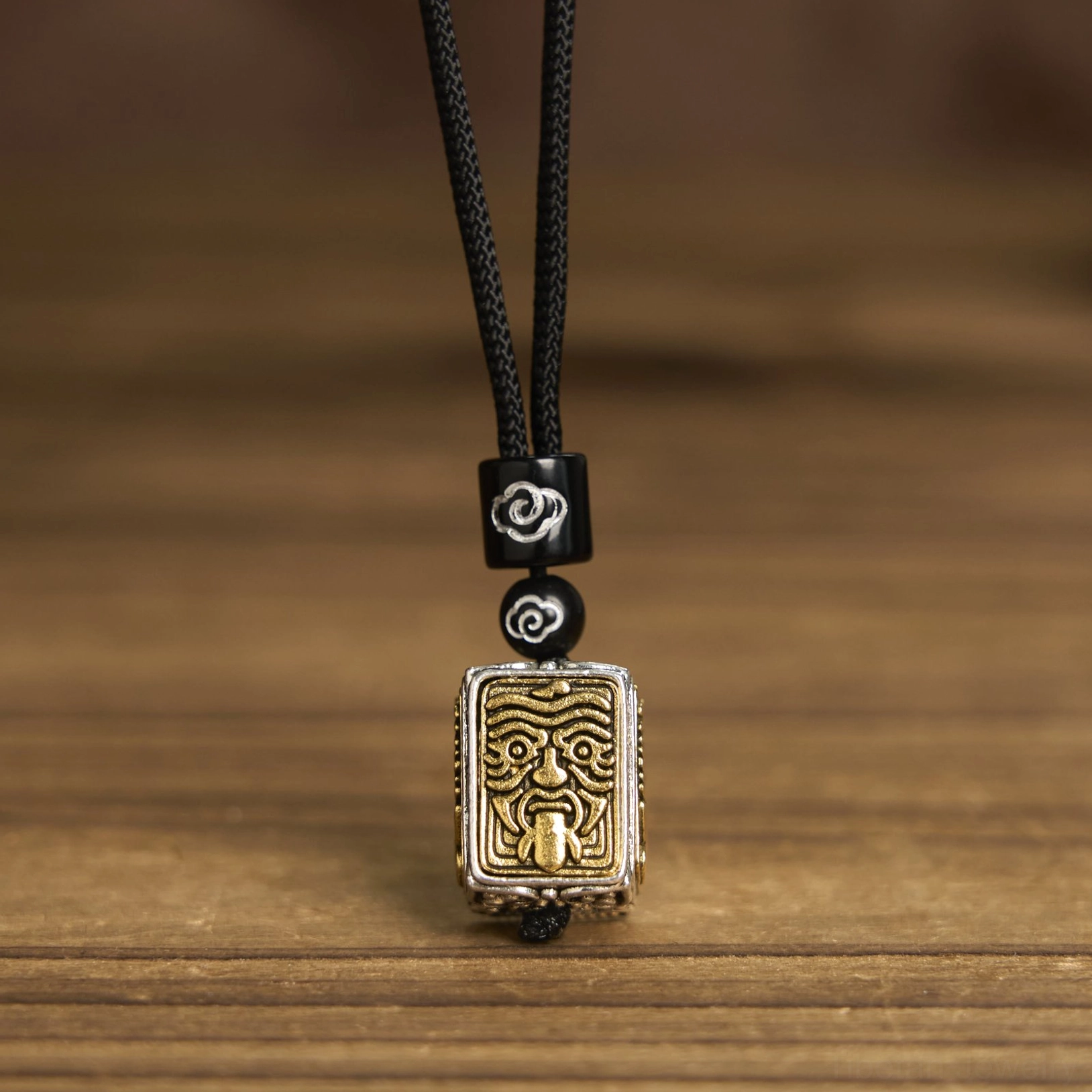 Zakiram tibetan protective deity pendant necklace front display, black woven cord with decorative spacer beads and square relief pendant on wooden surface