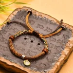 Zakiram goddess of wealth tibetan braided bracelet with wooden beads and metal charm on carved stone tray, flat lay top view