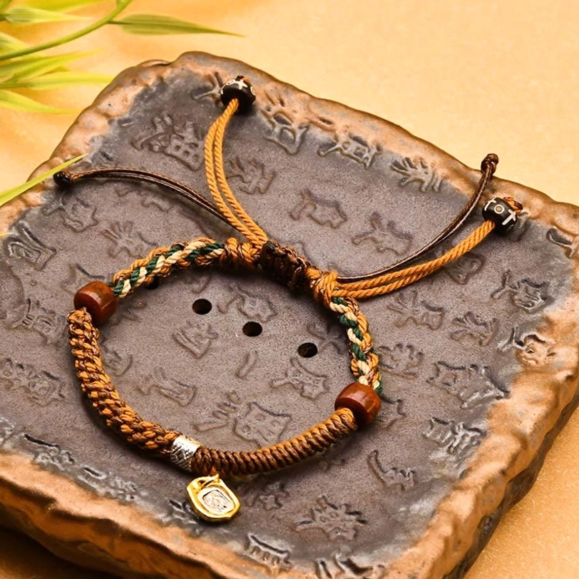 Zakiram goddess of wealth tibetan braided bracelet with wooden beads and metal charm on carved stone tray, flat lay top view