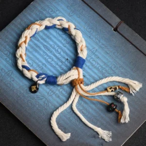 Zakiram Goddess of Wealth handmade braided lucky bracelet in tri-color design with copper charms on blue patterned notebook