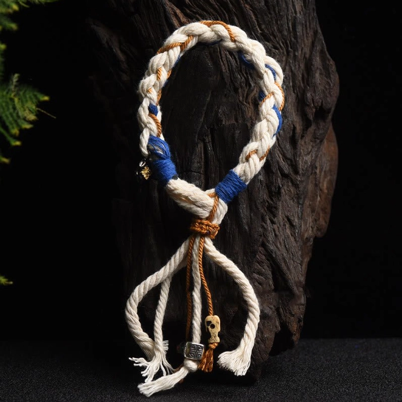 Zakiram Goddess of Wealth bracelet featuring twisted three-strand rope with tasseled ends and skull pendant on dark wood