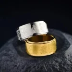 Dual-tone Chinese zodiac natal Buddha spinning ring with Heart Sutra engraving on dark stone surface, showing three-quarter view
