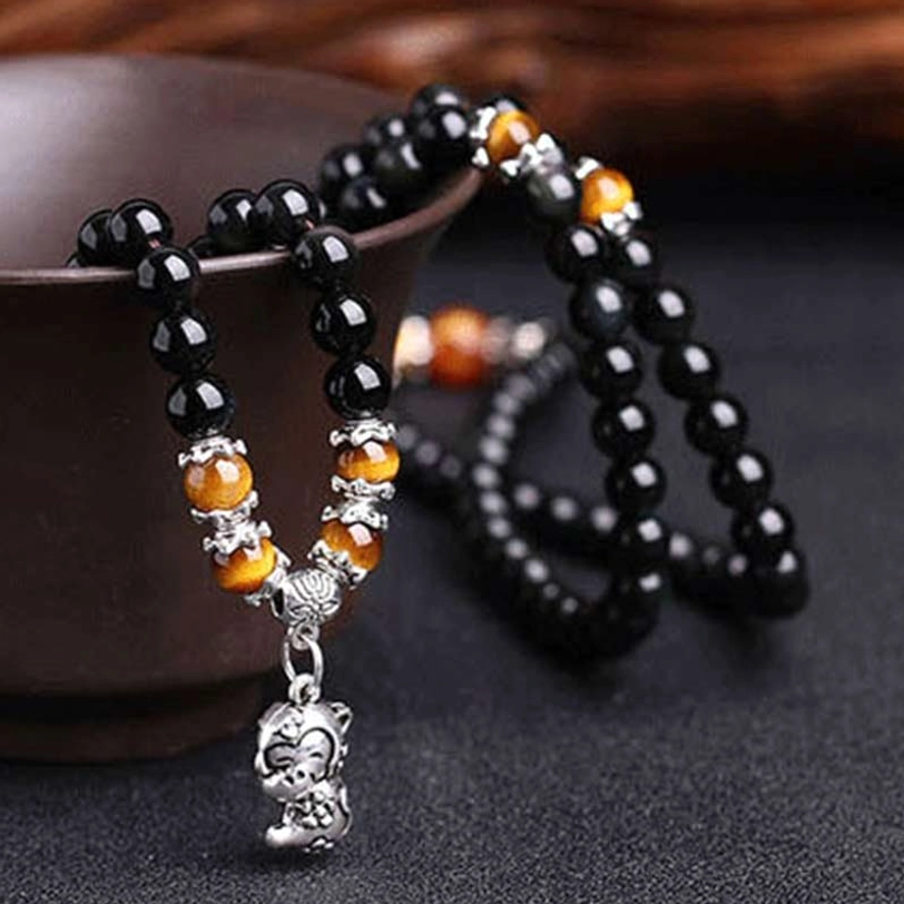Black obsidian mala bracelet with tiger eye beads and monkey zodiac silver pendant in ceramic bowl, eye-level view