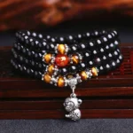 Black obsidian and tiger eye 108 bead mala bracelet with monkey zodiac silver charm, overhead view on wooden surface