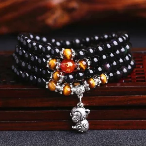 Black obsidian and tiger eye 108 bead mala bracelet with monkey zodiac silver charm, overhead view on wooden surface