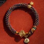 Chinese zodiac natal Buddha braided bracelet with mixed-color woven rope, gold metal charms and Sanskrit pendant, flat lay